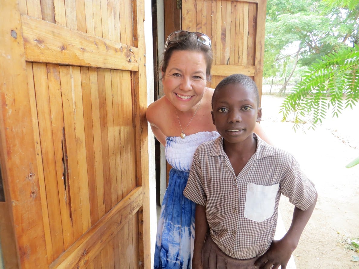 An adult woman standing beside a Kenyan boy outside.