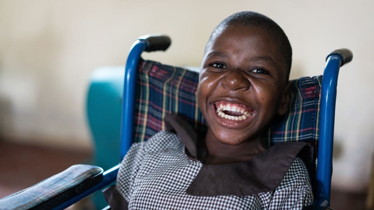 A Kenyan child with a bright smile sitting in a blue wheelchair.