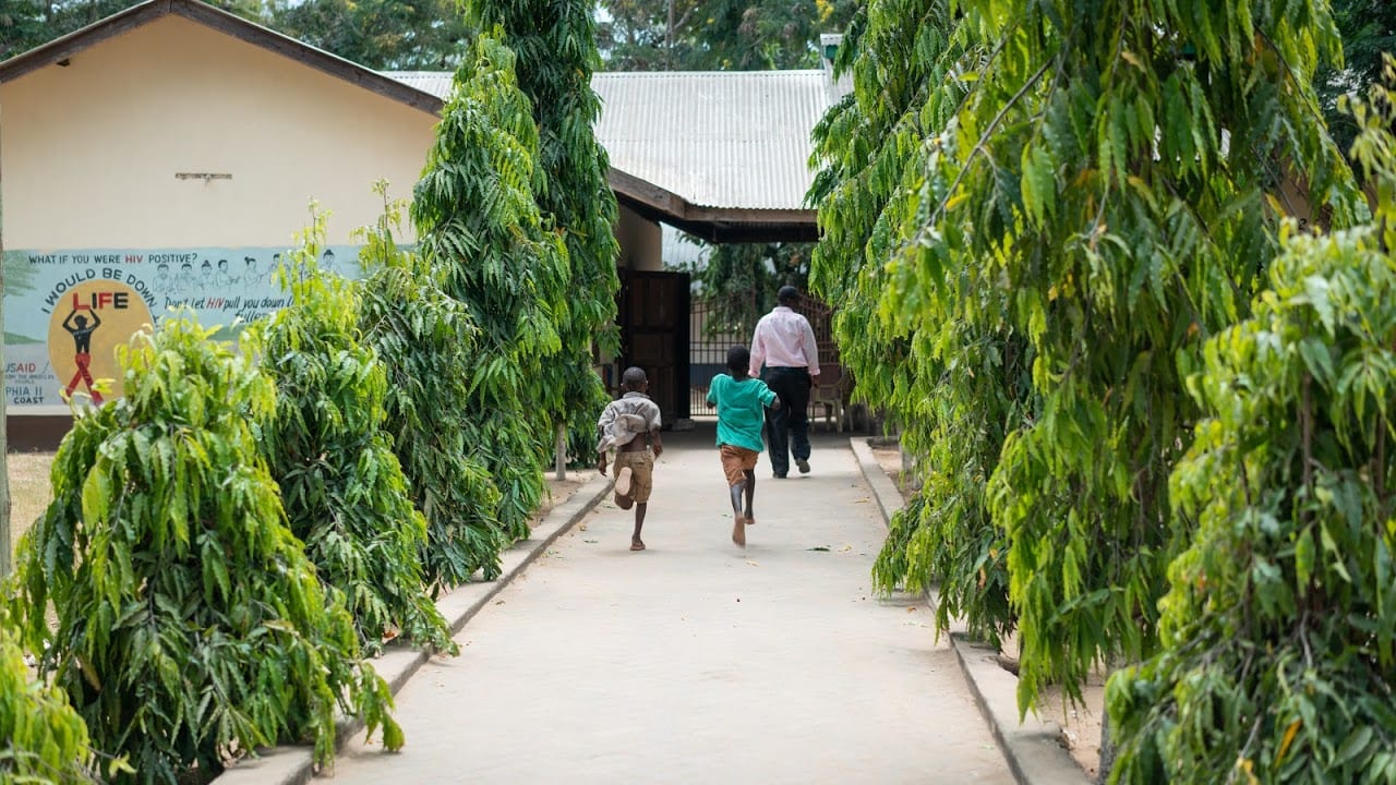 Two children and an adult male running down an outdoor pathway towards a building.