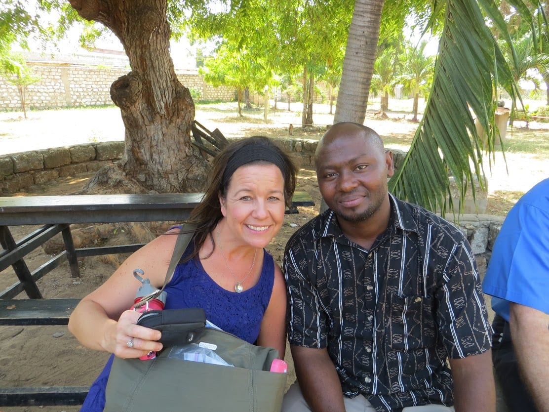 An adult woman and a Kenyan male sitting beneath a tree.