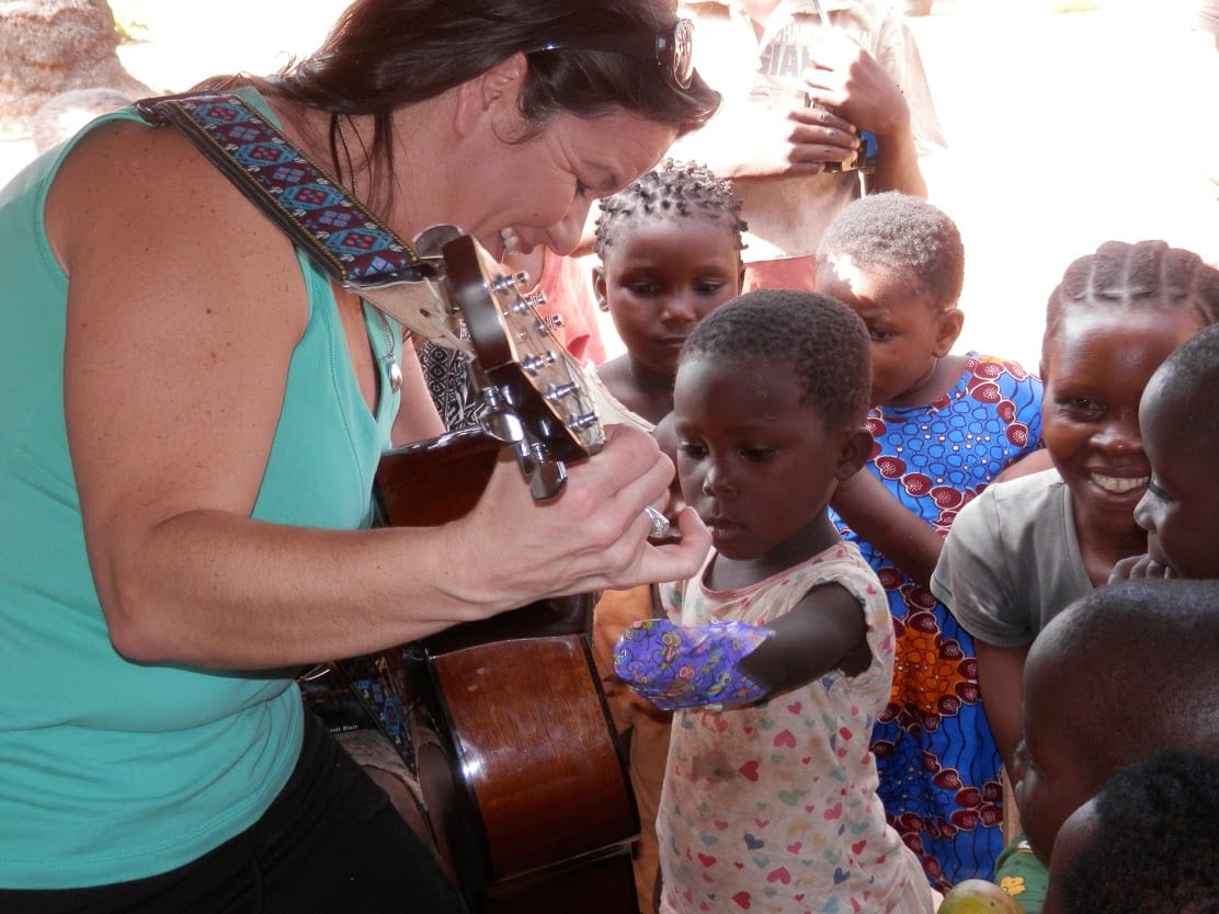 A woman showing a group of young children who to play the guitar.