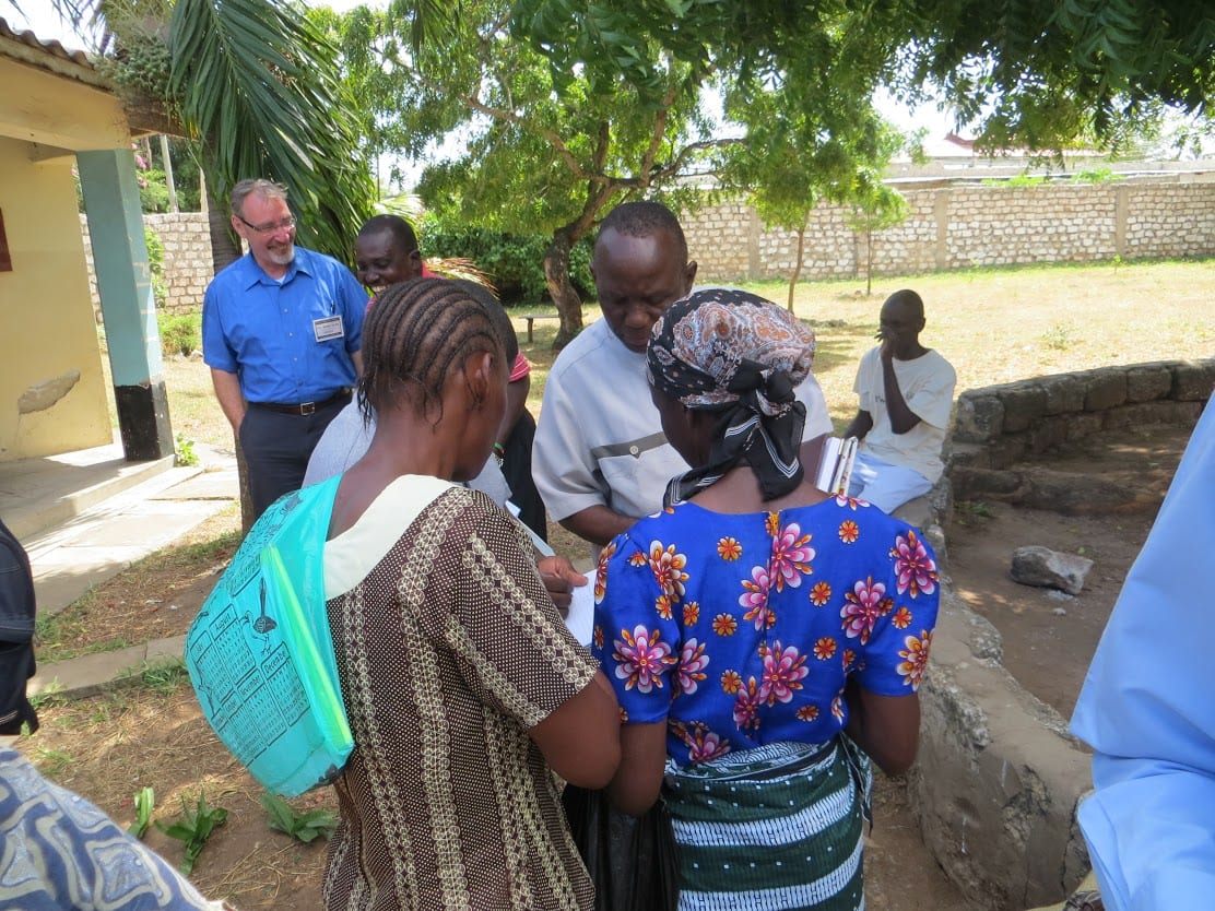 A man and two children stand outside, looking down at a piece of paper.