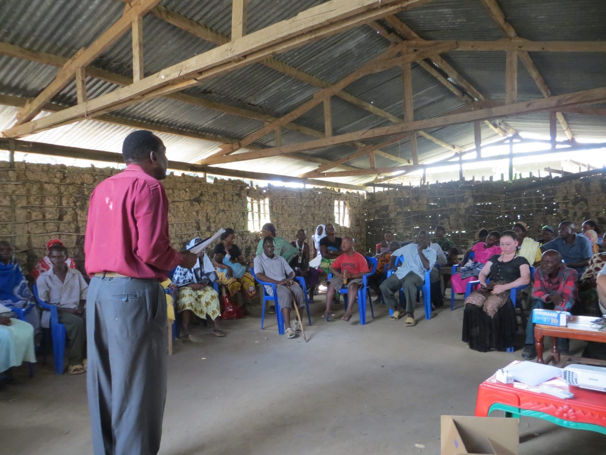 An adult man standing, speaking to a crowd of listening adults