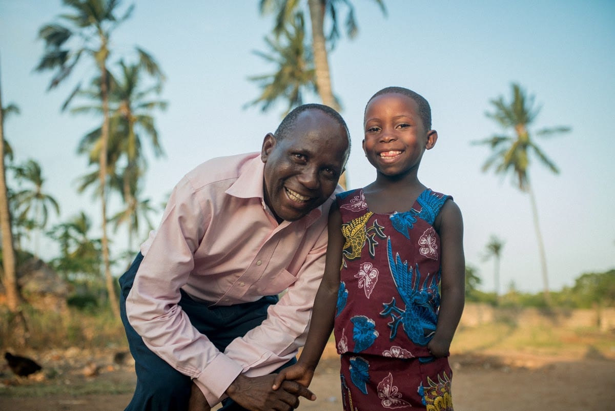 A Kenyan male standing outside, beside a young Kenyan boy.