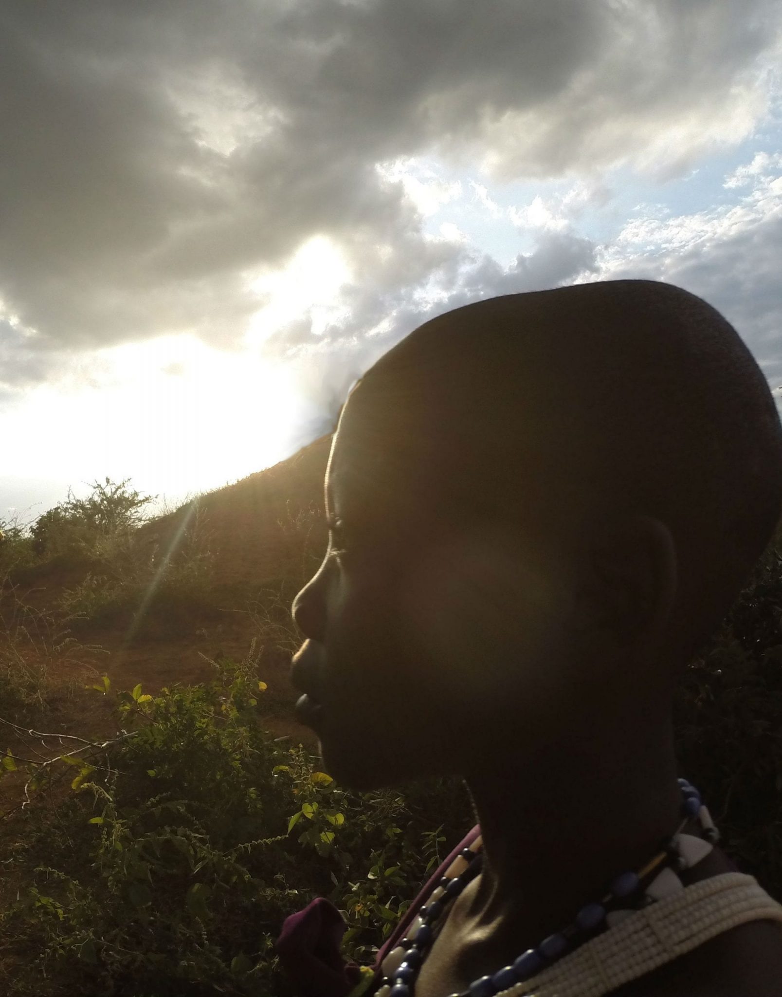 A Kenyan child looking into the distance with the sun shining behind them.