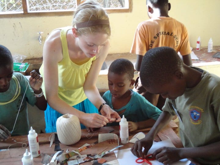 A blonde woman helping a young child with an arts and crafts project.