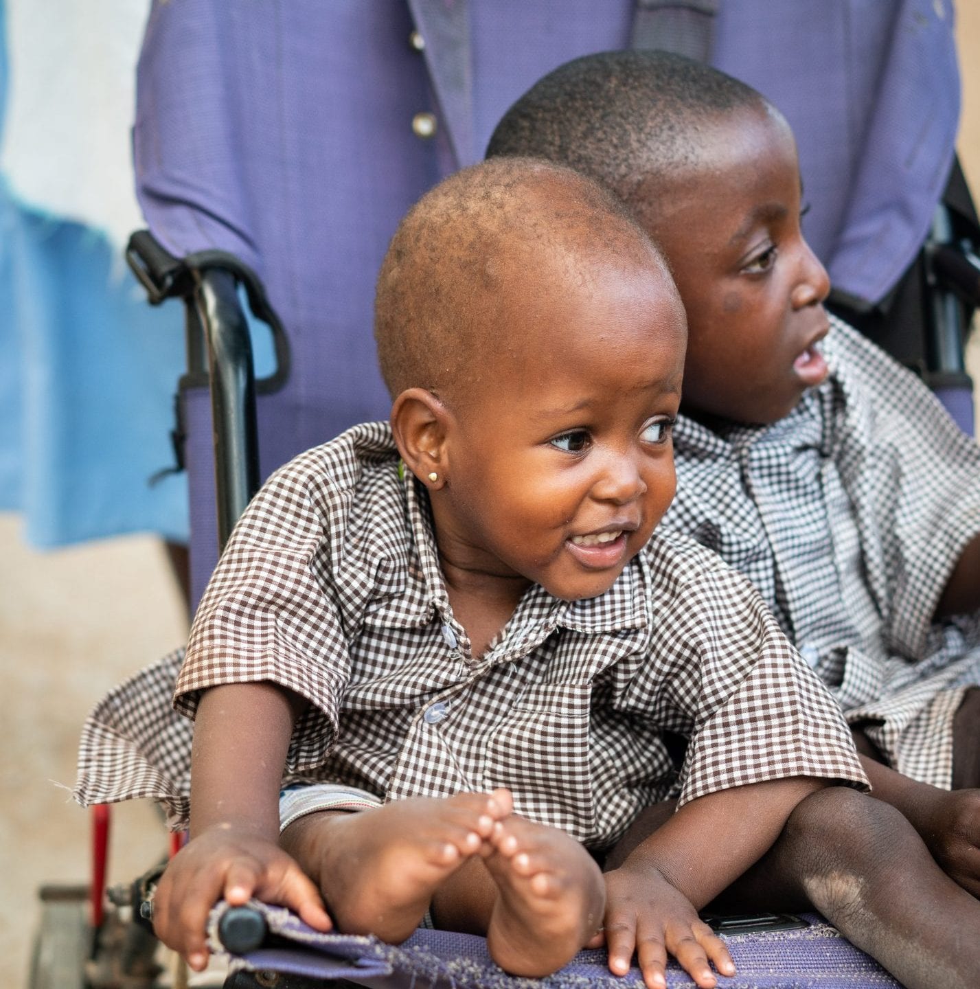 Two young Kenyan children wearing plaid shirts, sitting in a blue chair.