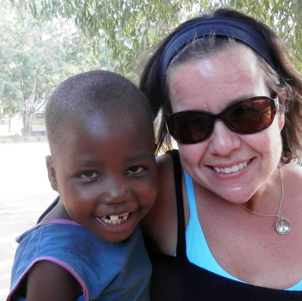 A brunette woman wearing sunglasses holding a smiling Kenyan child.