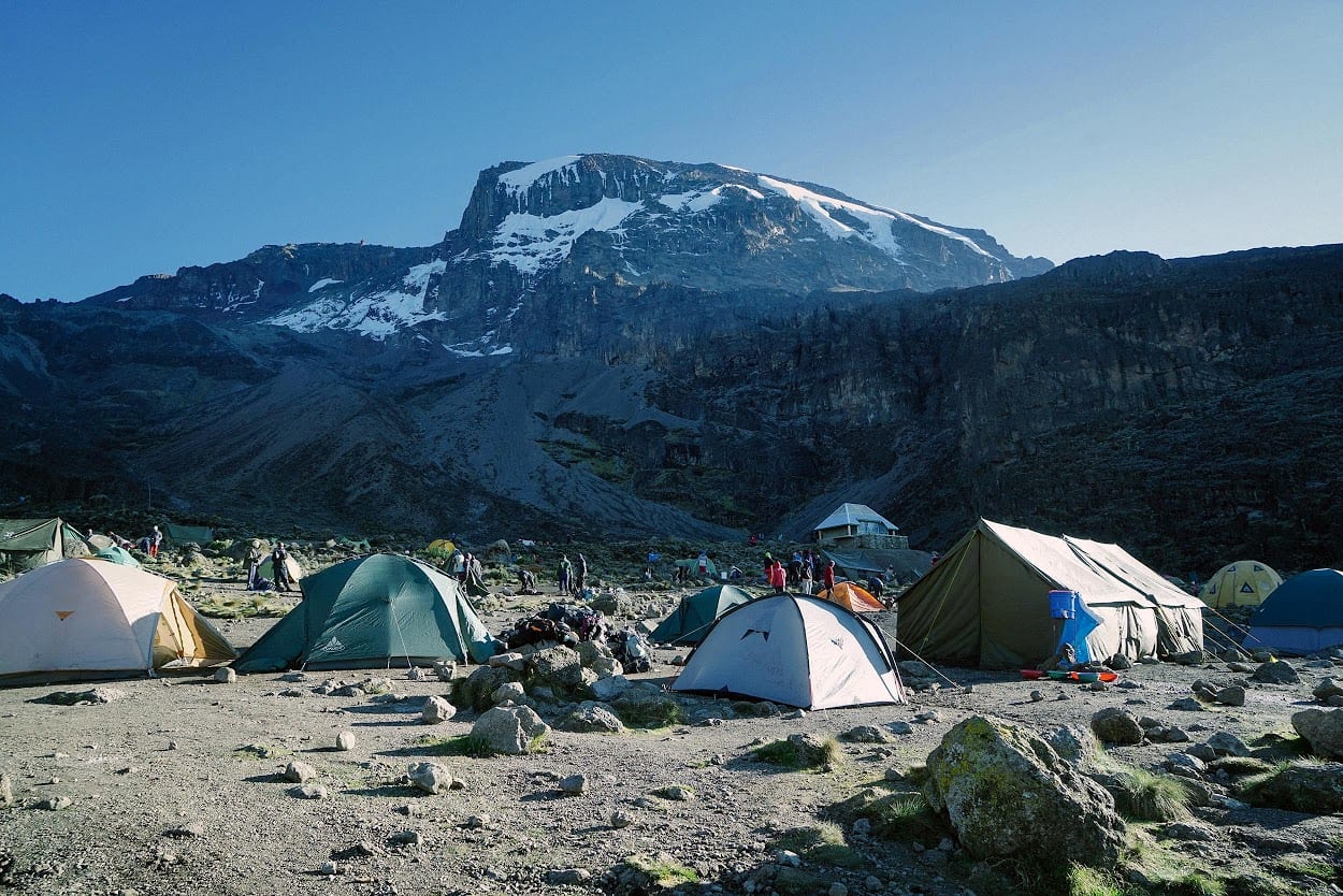 A scenic photo of 9 tents pitched at the base of a mountain.