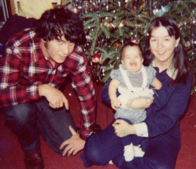 A photo of a a man and a woman holding a baby sitting before a decorated Christmas tree.