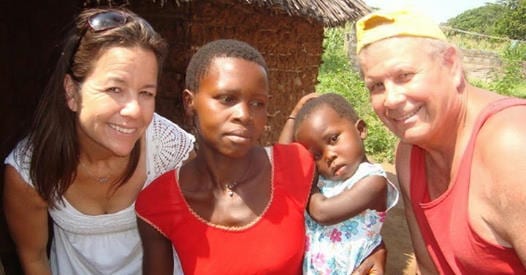 A man wearing a yellow hat and a woman wearing a white shirt standing beside a Kenyan woman holding a baby.