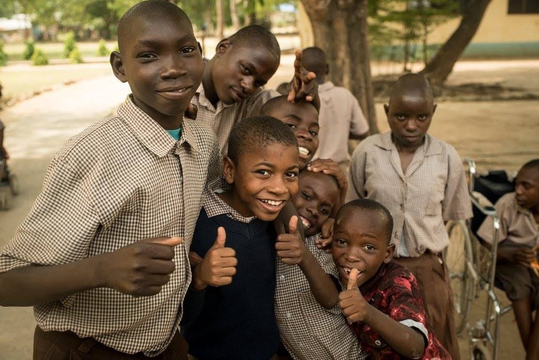 9 Kenyan boys looking at the camera, smiling, holding a thumbs up.
