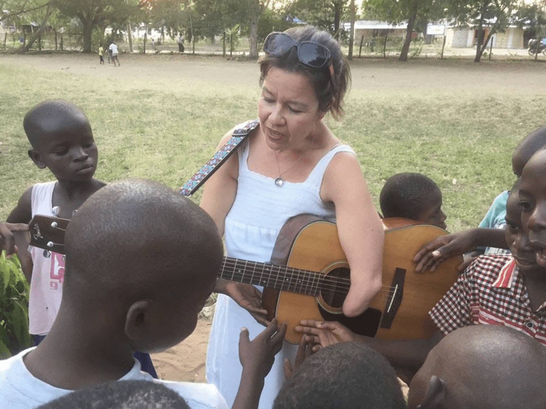 An adult woman showing a group of boys how to play guitar.