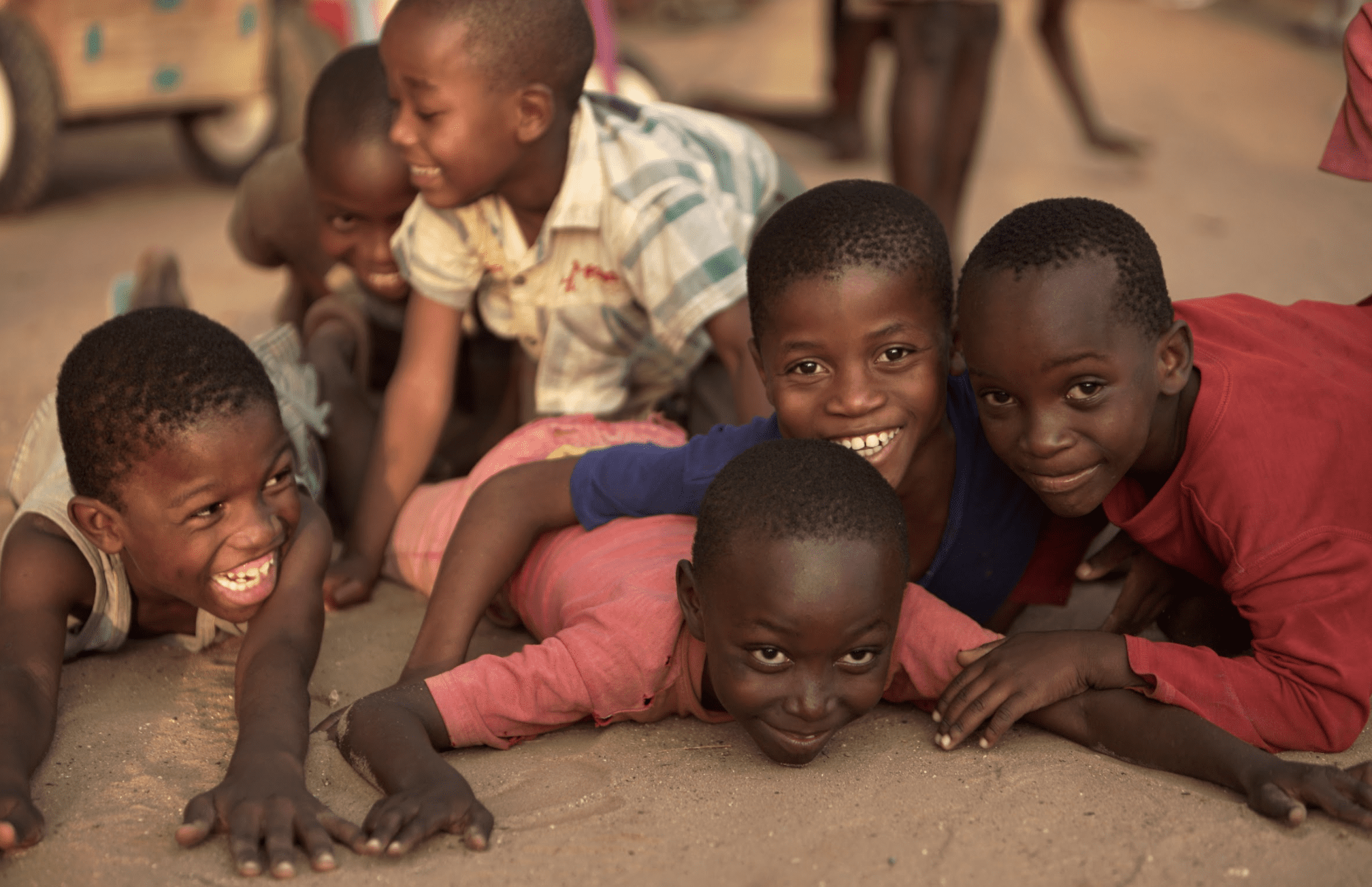 6 young Kenyan boys laying on the floor together and laughing.