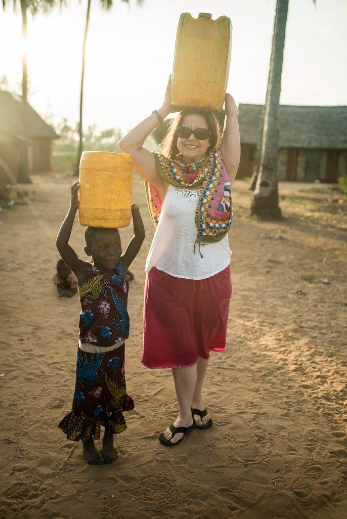 A adult female and a young Kenyan girl holding large containers of water above their heads.