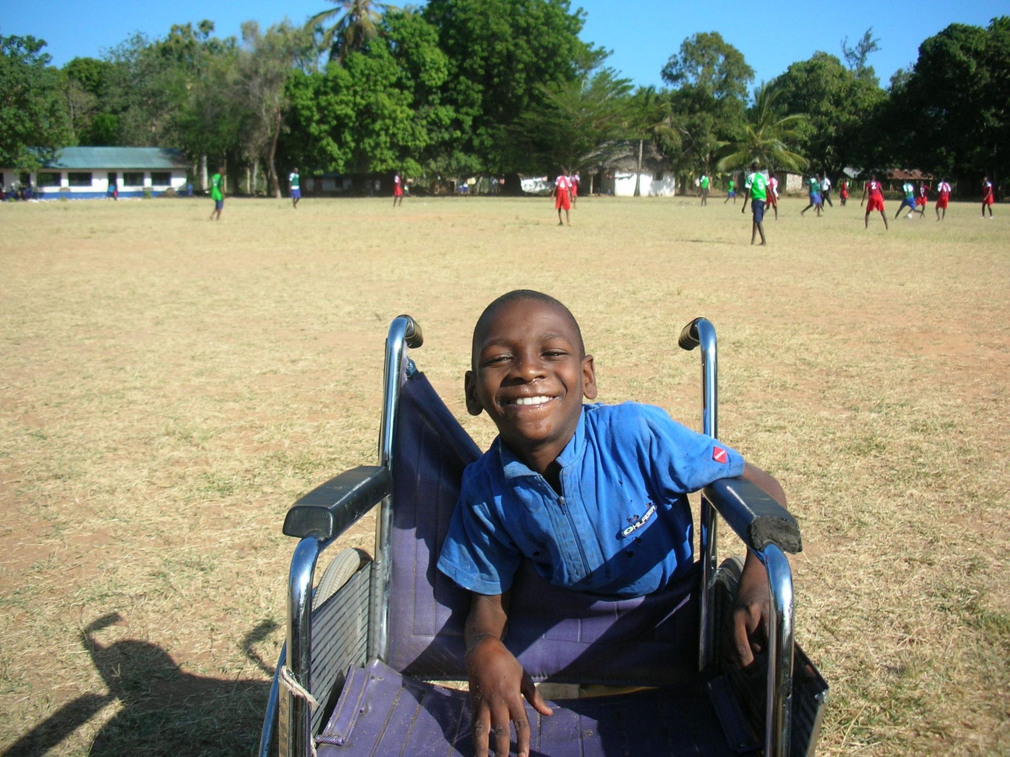 A Kenyan boy smiling and leaning on a wheelchair.