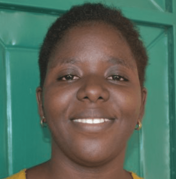 A Kenyan woman wearing a yellow shirt, standing in front of a green door.