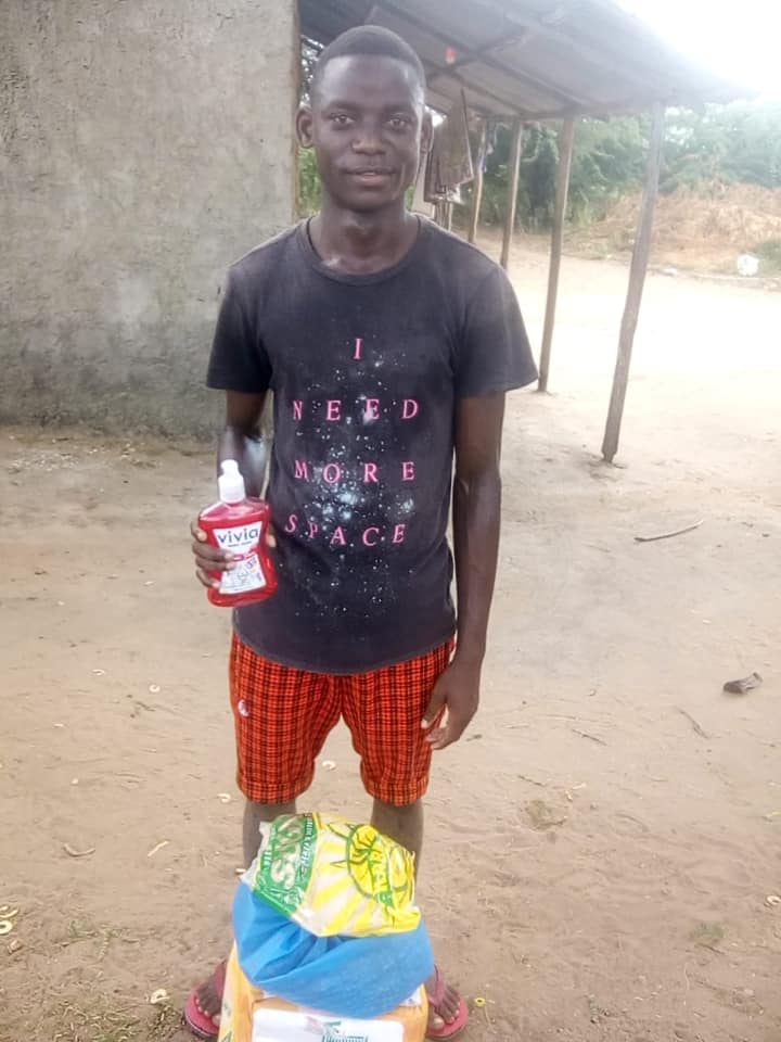 A teenage male standing outside with a bottle in his hand and a stack of bags laying at his feet