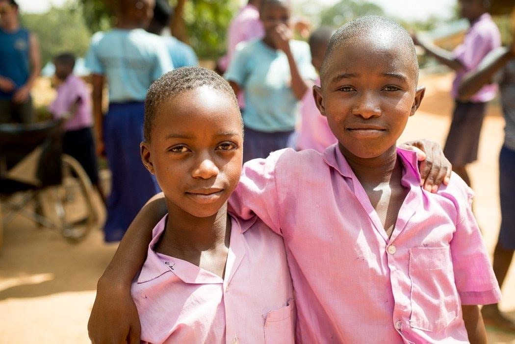 Two young Kenyan boys wearing matching purple collared shirts. They each have their arm around each other.