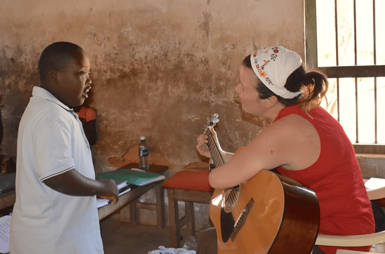 An adult woman playing guitar with a Kenyan boy.