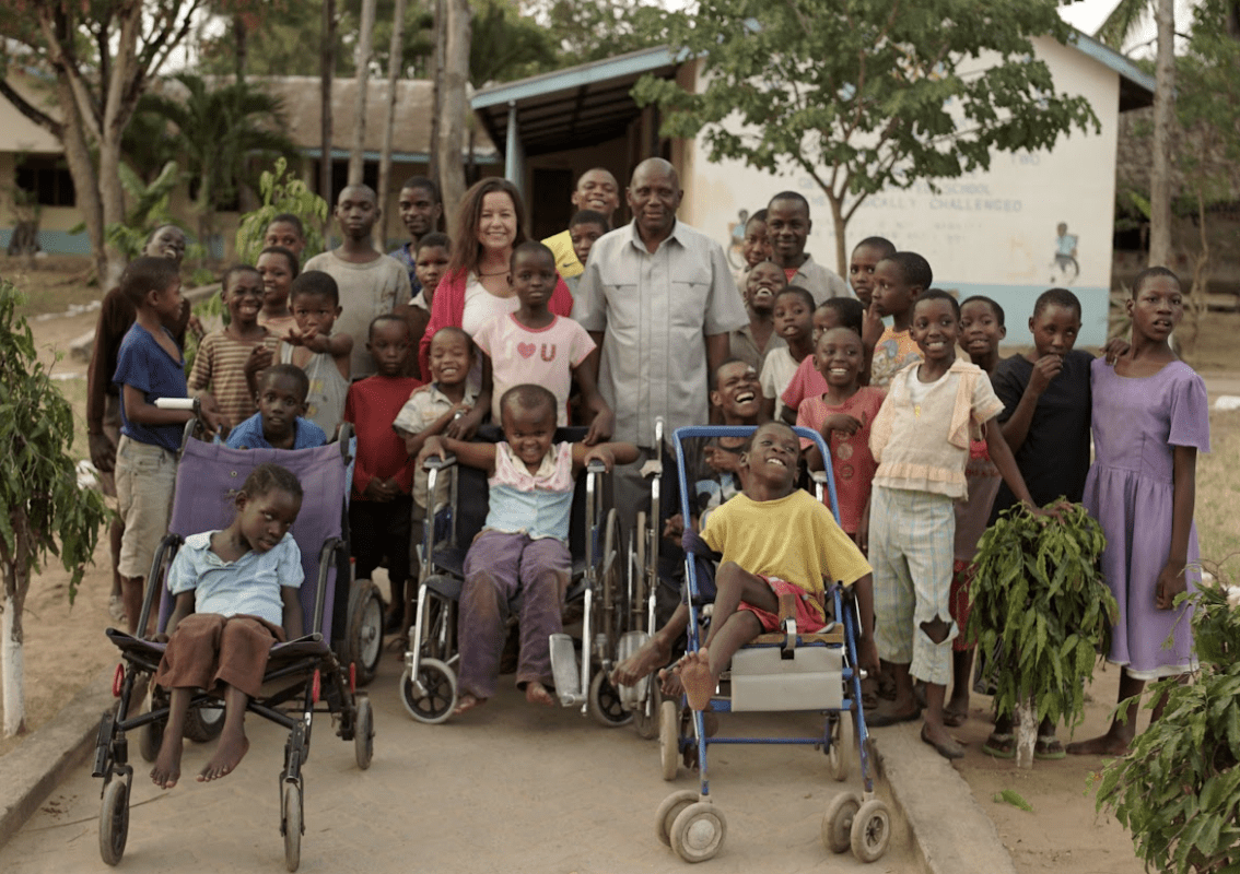 An adult man and woman surrounded by 20 school children.