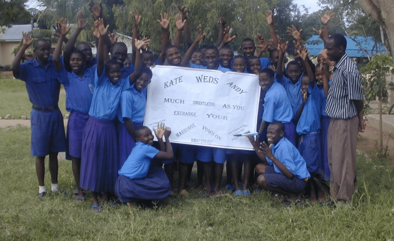 22 children in blue school uniforms standing around a small white banner.