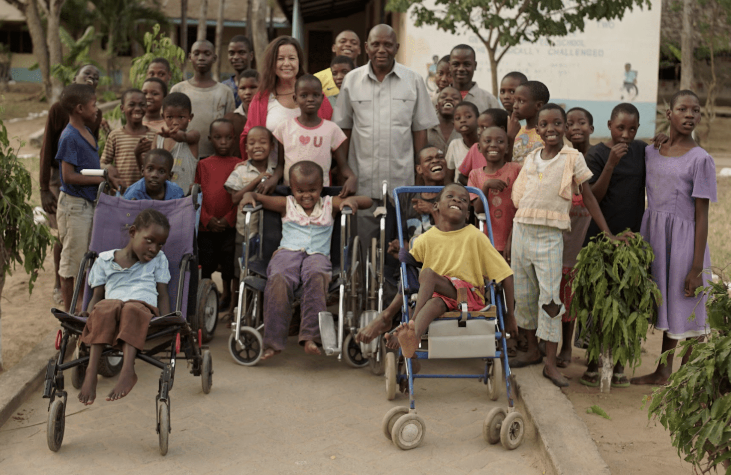 An adult man and woman surrounded by 20 school children.