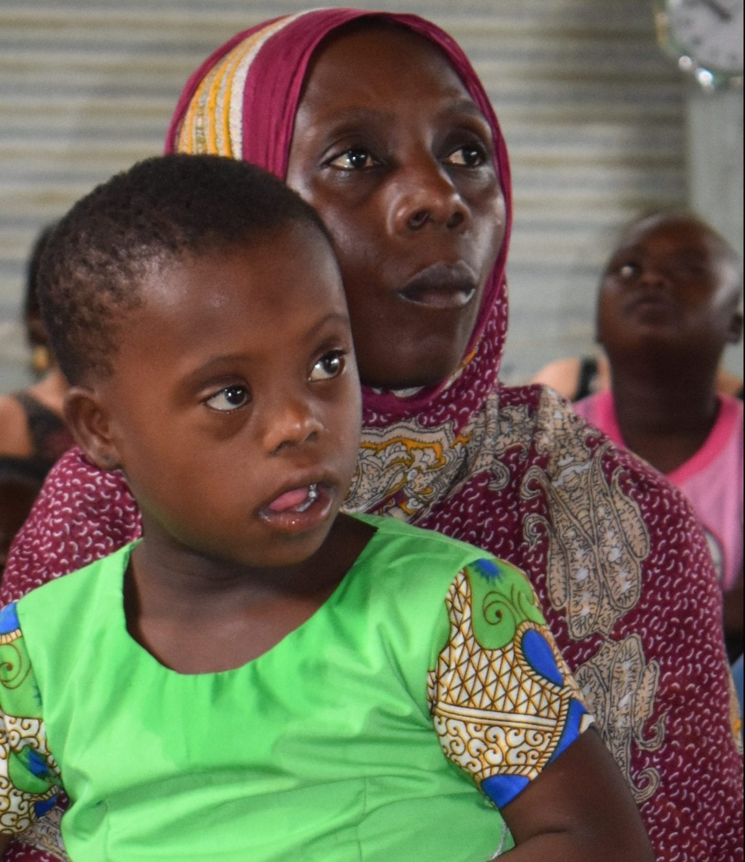 A Kenyan mother holding a child wearing a green top.