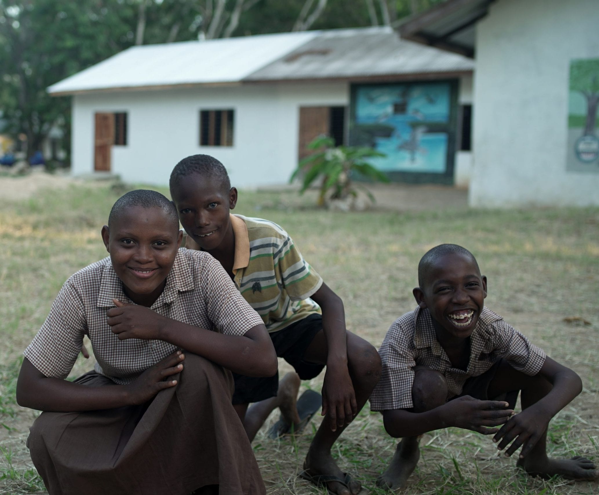 Three Kenyan boys who are squatted above the ground.