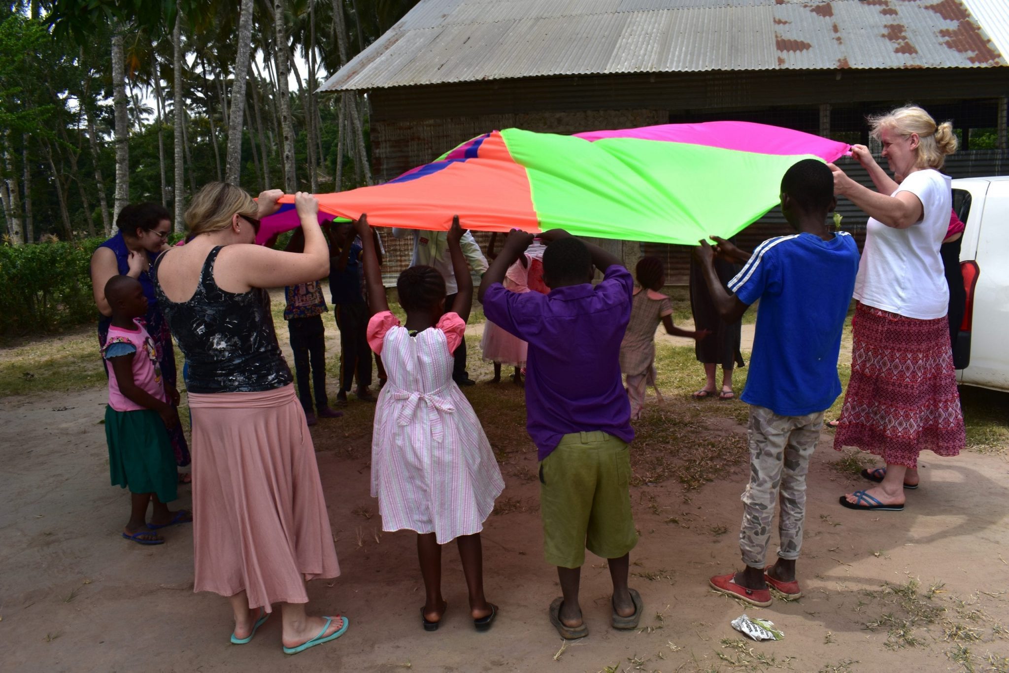 A group of teachers and Kenyan school children playing outside with a parachute.