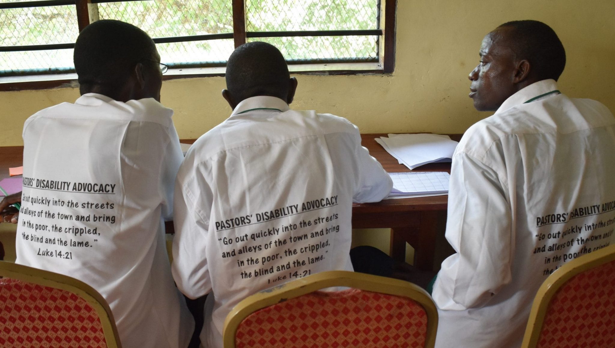 Three Kenyan adults seated at a table looking at papers.