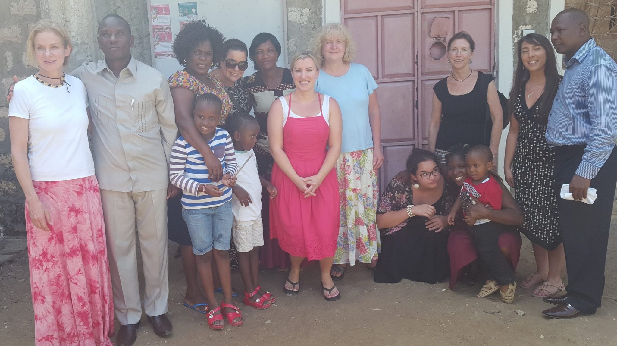 A group of 15 peoples of various ages standing outside smiling at the camera.