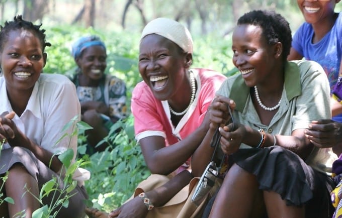 Group of Kenyan women laughing outside, surrounded by greenery