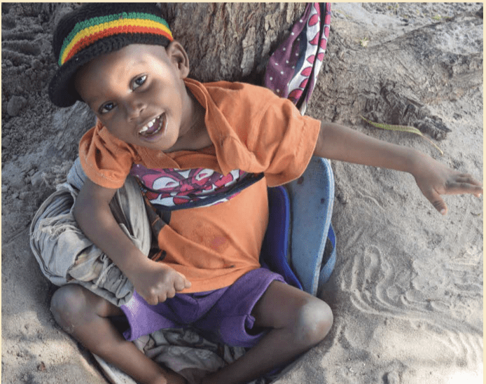 A photo of a young Kenyan boy, Emmanuel, smiling as he sits in the sand.