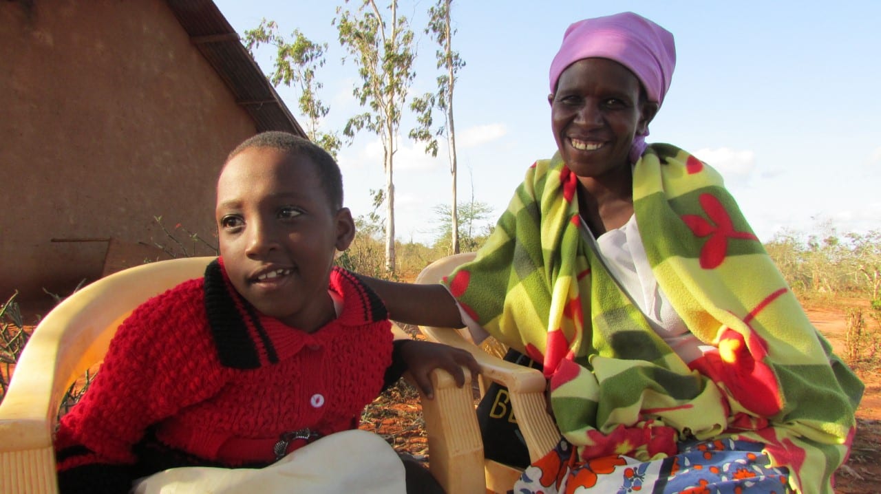 A Kenyan woman and a child sit by each other outside