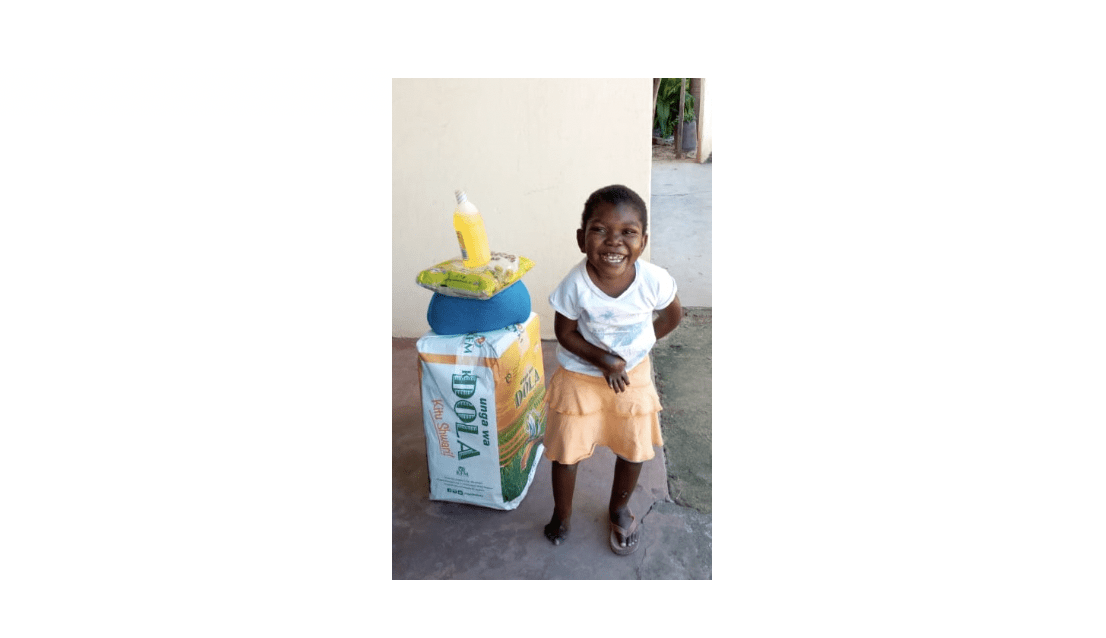 Young girl smiling next to packages received from Kupenda's food relief program