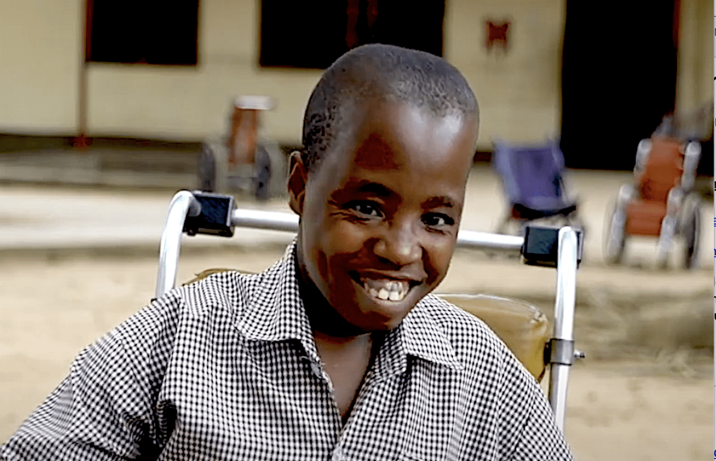 Kasere wearing gingham shirt, smiling, sitting in wheelchair.