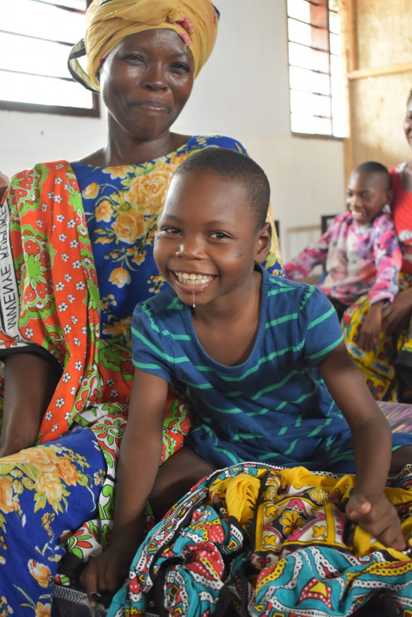 Smiling young child sitting on mother's lap, wearing bright colorful clothing.