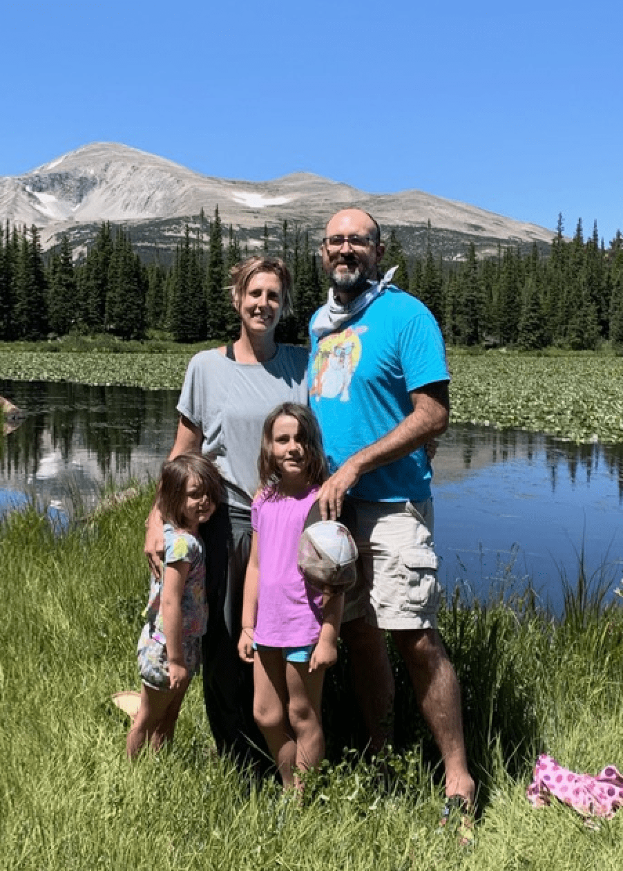 Jon and Heidi Busch with their two daughters- standing in front of a mountain landscape.
