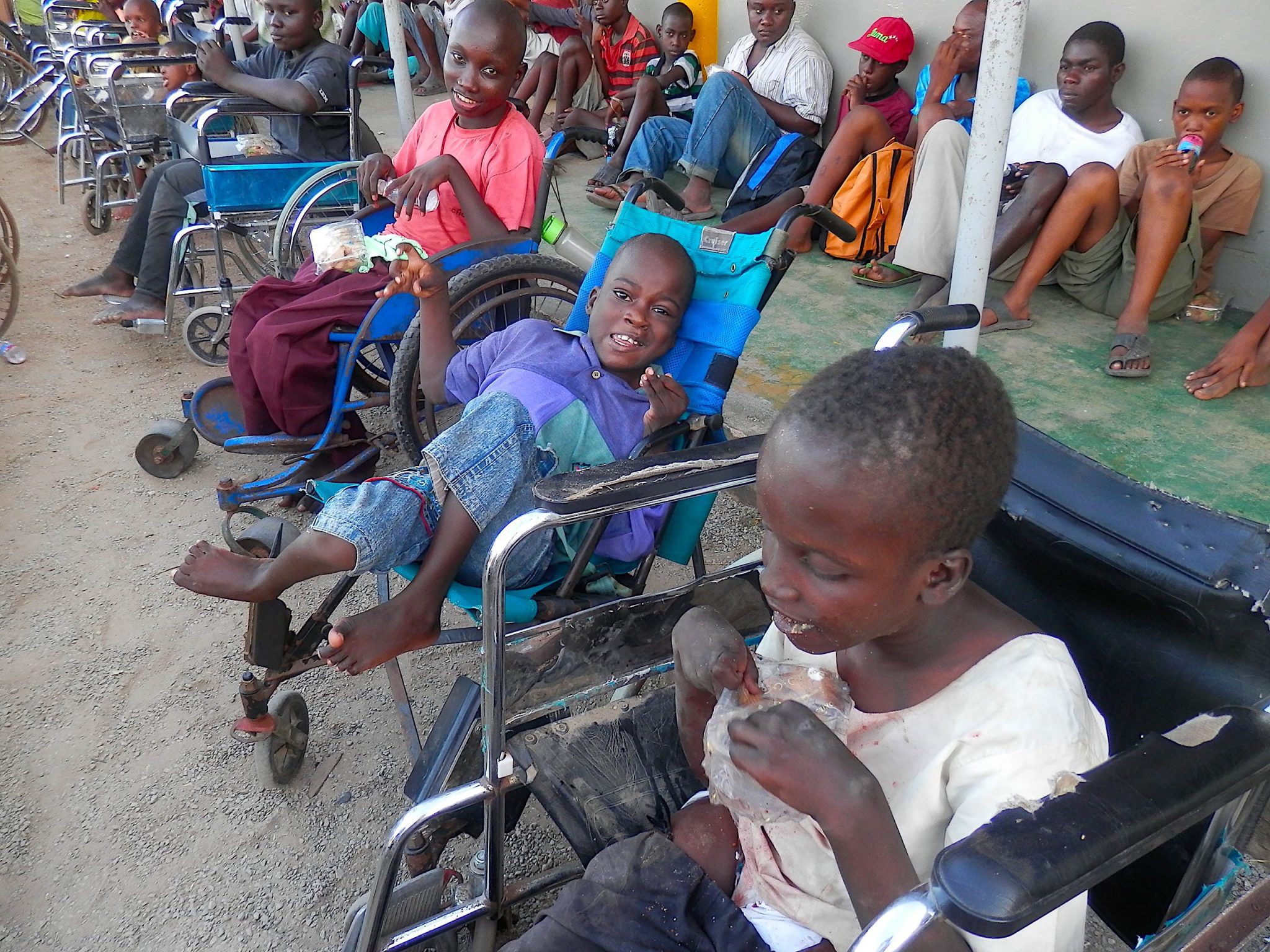 Two long rows of Kenyan boys. Three young boys in wheelchair are most prominent in the photo.