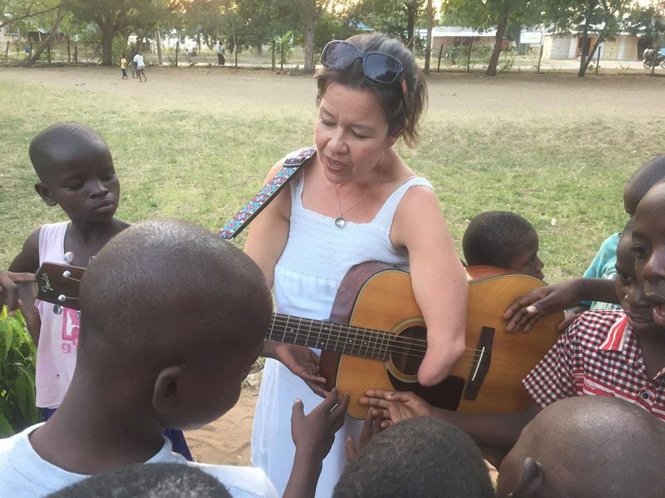 A woman playing guitar for a group of interested young boys