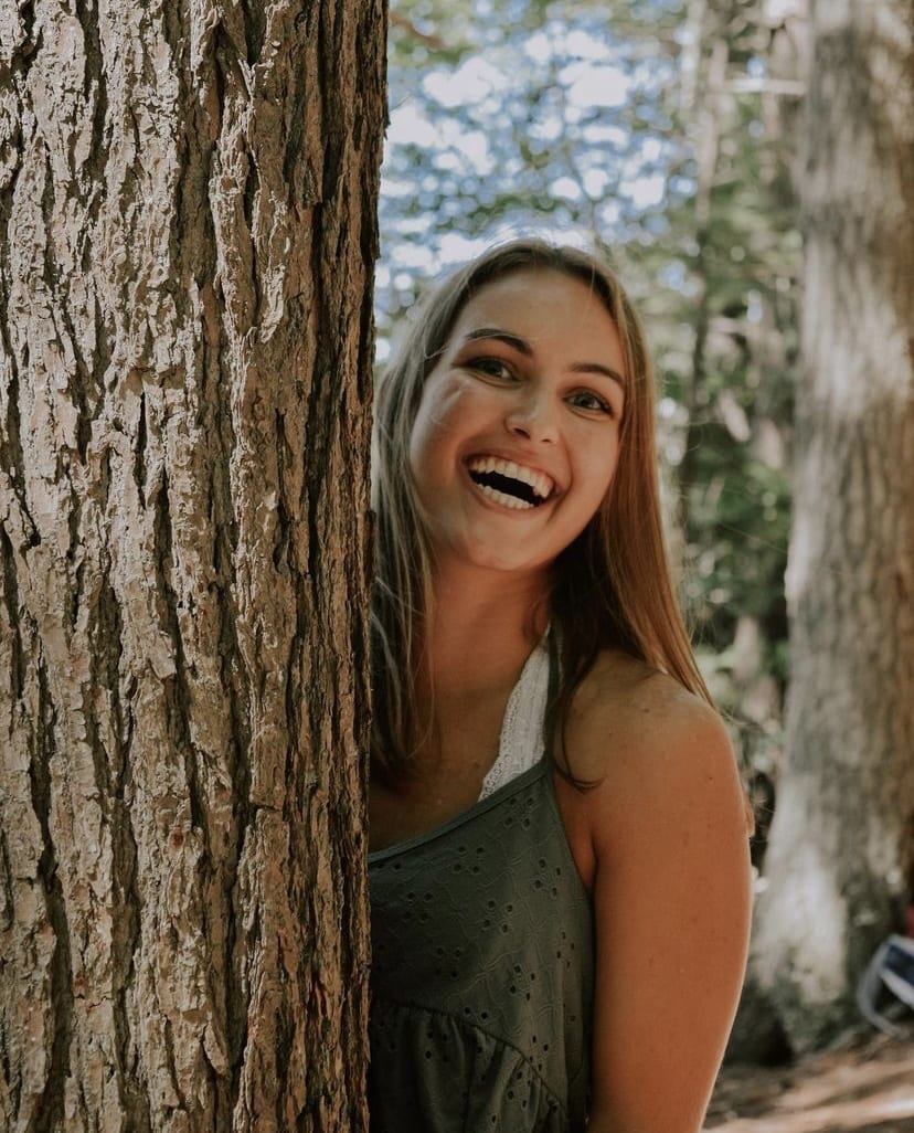 Girl smiling, standing beside a tree