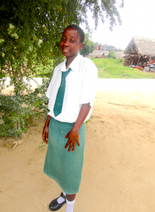 A girl standing outside, wearing a white shirt, green skirt, and green neck tie.