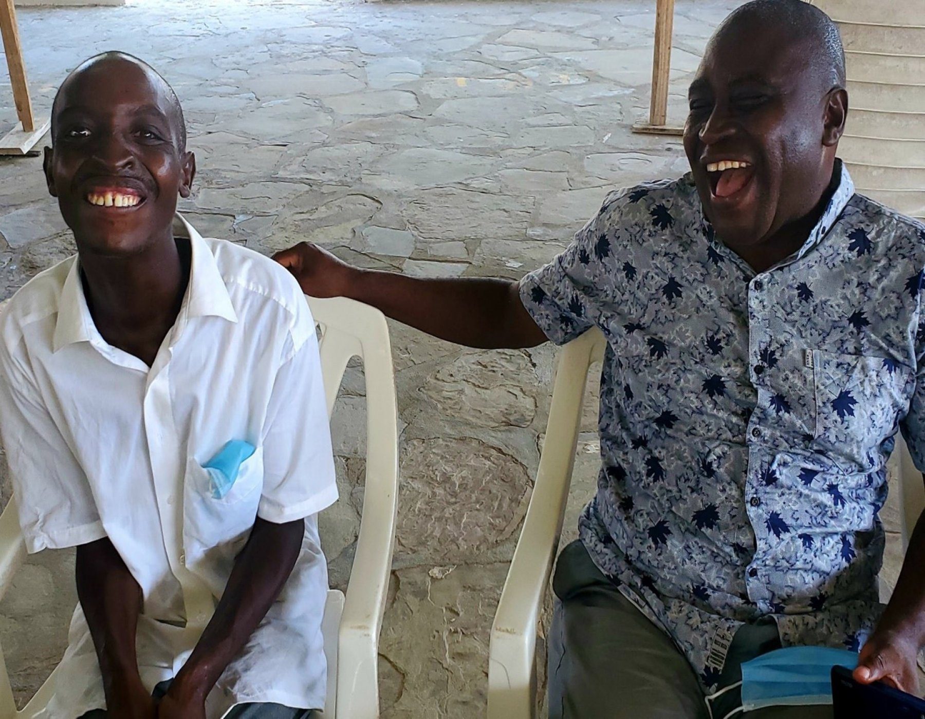 A young man and an adult man seated beside each other, laughing.