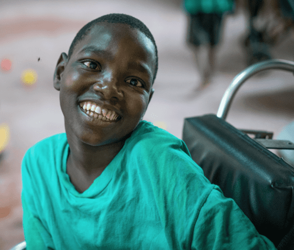 A child in a green shirt, seated in a wheelchair smiling. 