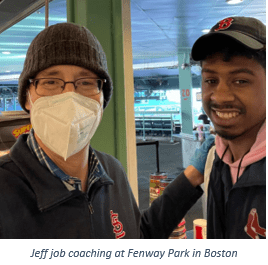 A man wearing a hat and a mask standing beside a young man smiling at Fenway Park in Boston, MA. 