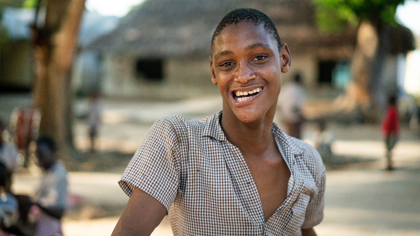 A teenage boy in a brown shirt standing outside and smiling.