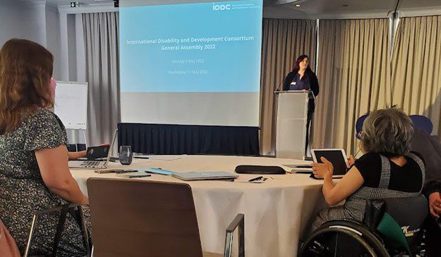 A female speaker standing at a podium and talking to an audience.