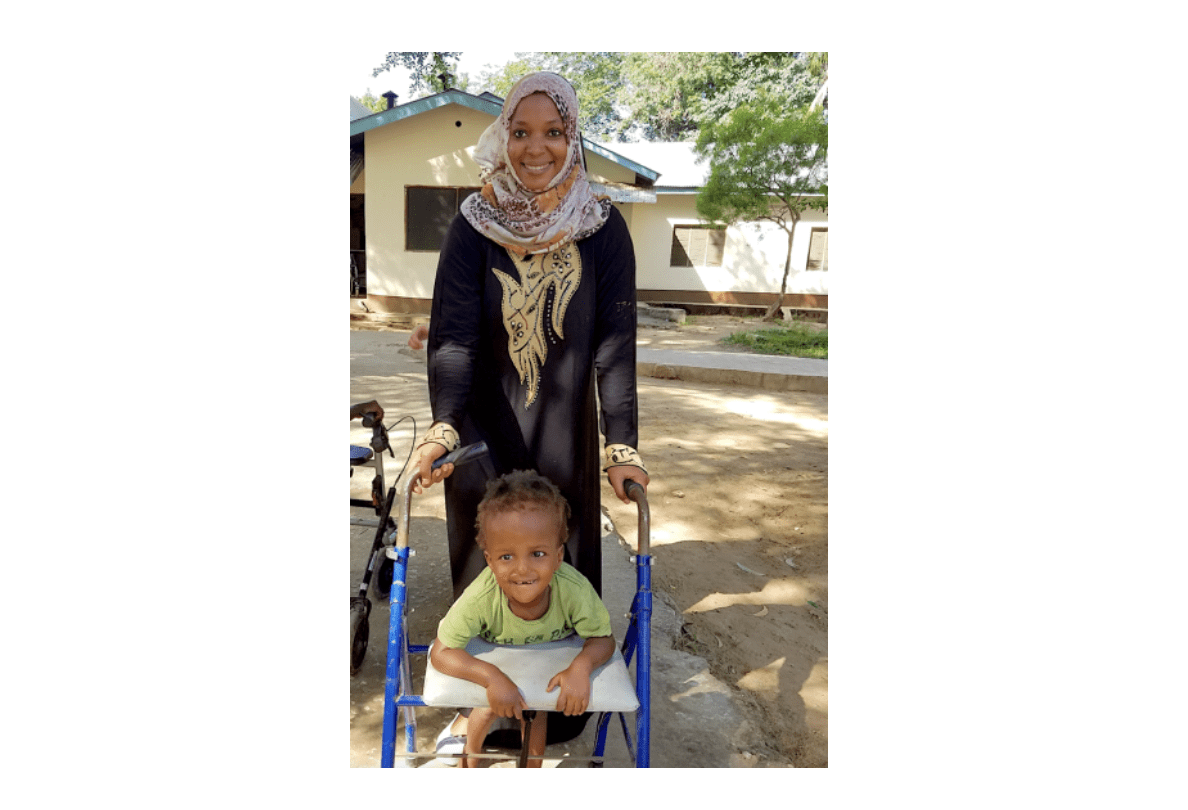 A woman smiling and pushing a young boy in a wheelchair.