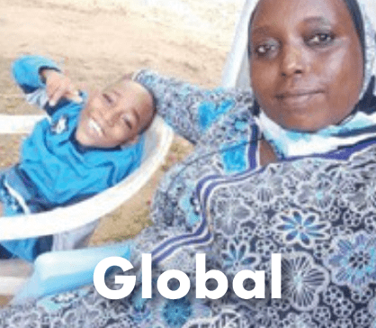 A woman wearing a blue and white patterned headscarf holding a child wrapped in a blue blanket, labeled "Global."